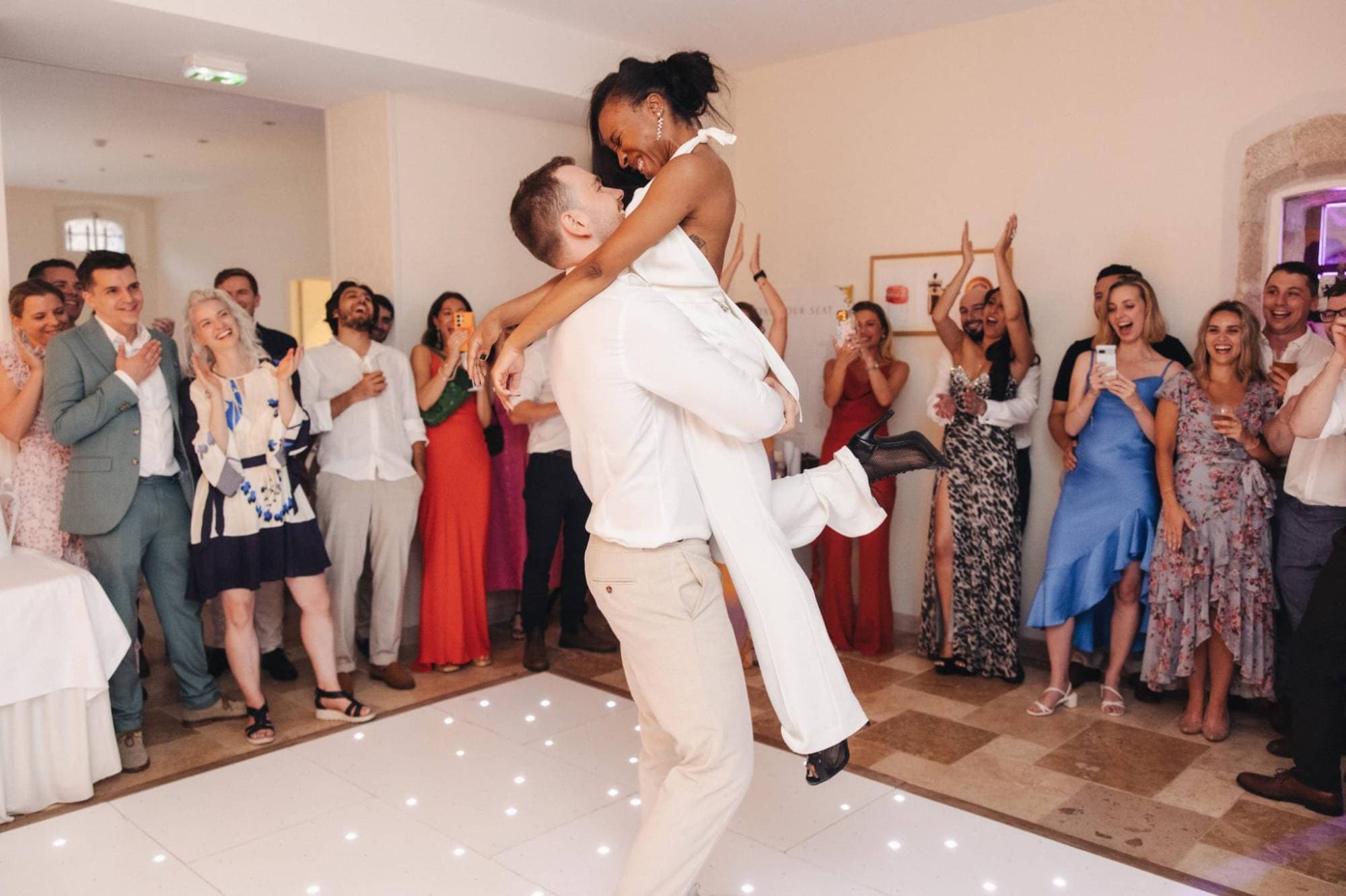 A groom lifting the bride during their first dance as the guests around the dance floor applaud